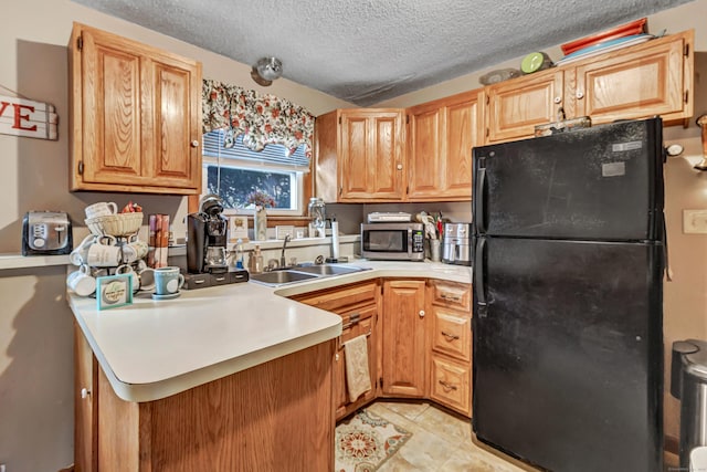 kitchen with a textured ceiling, sink, black fridge, kitchen peninsula, and light tile patterned floors