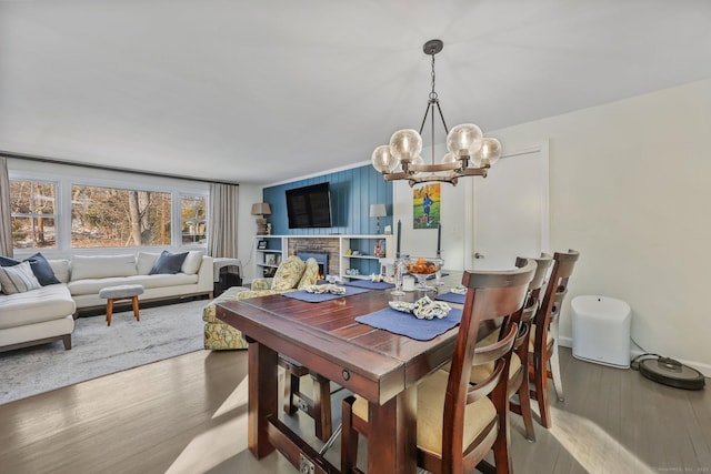 dining space featuring hardwood / wood-style flooring, a stone fireplace, and an inviting chandelier