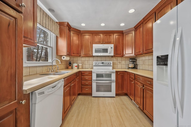 kitchen with decorative backsplash, sink, white appliances, and light hardwood / wood-style flooring