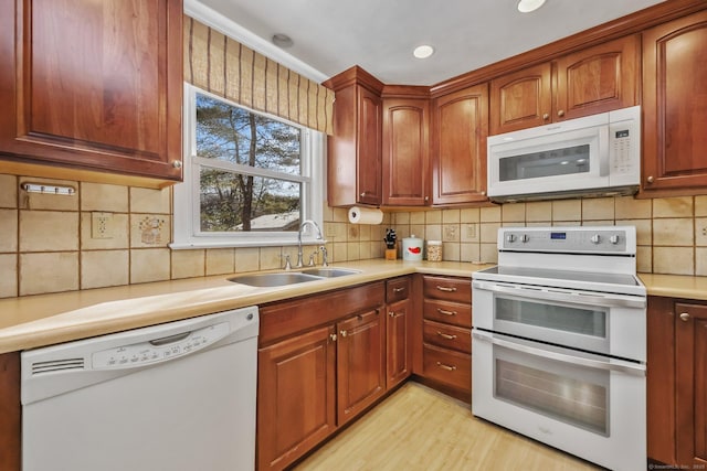 kitchen with sink, white appliances, tasteful backsplash, and light wood-type flooring