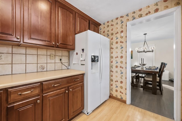 kitchen featuring light hardwood / wood-style floors, a chandelier, white refrigerator with ice dispenser, decorative light fixtures, and backsplash