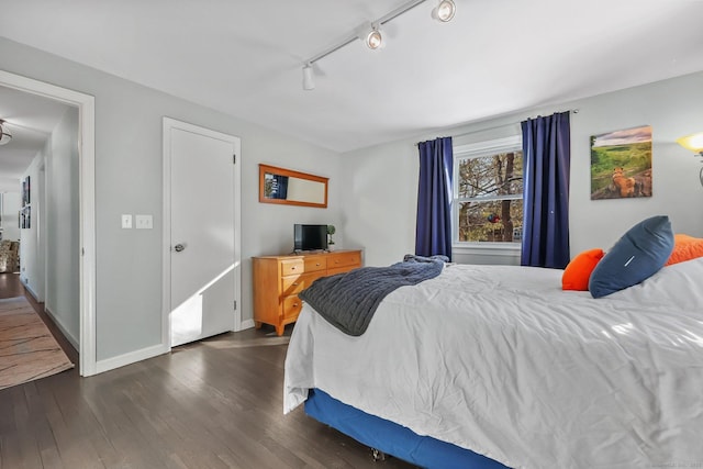 bedroom with rail lighting and dark hardwood / wood-style floors