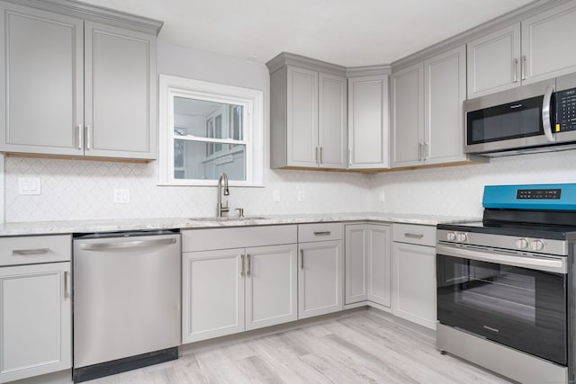 kitchen featuring stainless steel appliances, light hardwood / wood-style floors, light stone counters, and sink