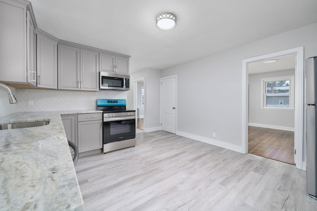 kitchen with appliances with stainless steel finishes, gray cabinetry, sink, light stone counters, and light hardwood / wood-style flooring