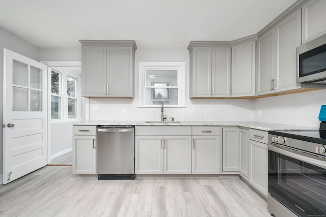 kitchen featuring sink, light stone counters, stainless steel appliances, and light hardwood / wood-style flooring