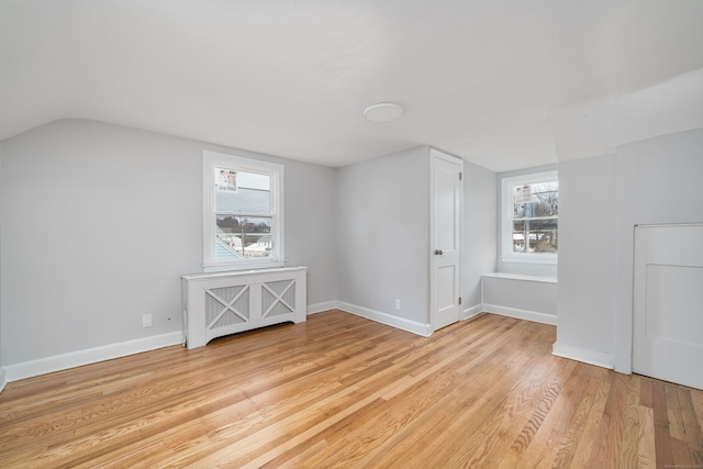 additional living space featuring radiator, light wood-type flooring, vaulted ceiling, and a wealth of natural light