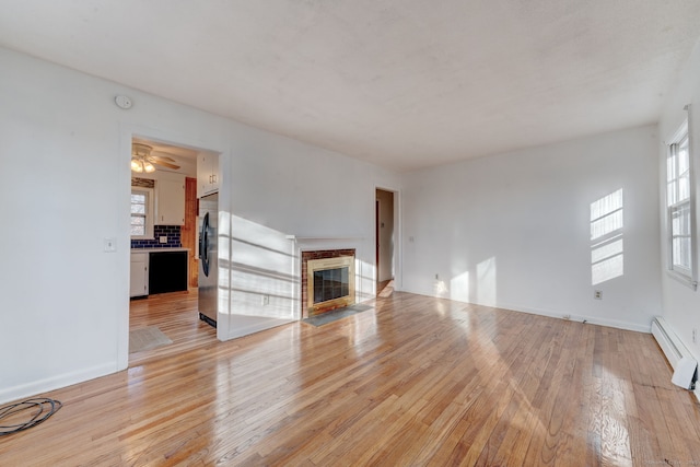 unfurnished living room featuring ceiling fan, light wood-type flooring, a high end fireplace, and baseboard heating