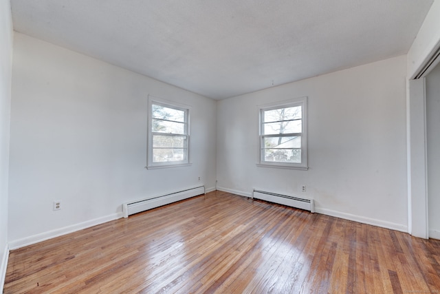 unfurnished room featuring baseboard heating and light wood-type flooring