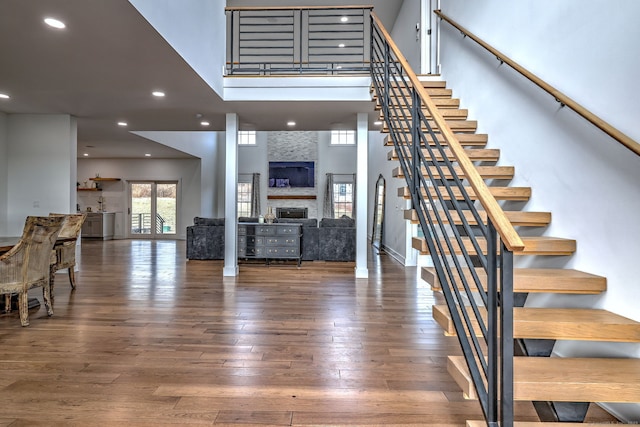 stairway featuring hardwood / wood-style flooring, a large fireplace, and a towering ceiling