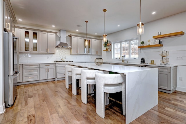 kitchen with pendant lighting, a breakfast bar, appliances with stainless steel finishes, a center island, and wall chimney exhaust hood