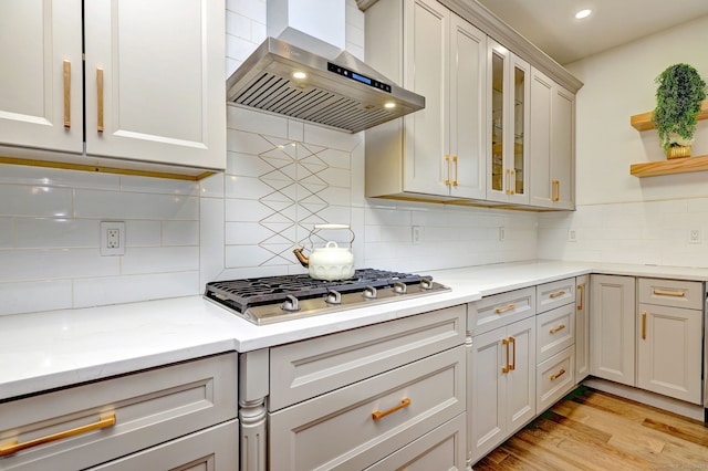 kitchen with tasteful backsplash, stainless steel gas cooktop, light stone counters, light hardwood / wood-style floors, and wall chimney range hood