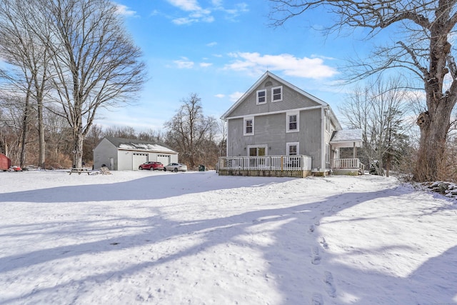 snow covered rear of property featuring a garage, an outdoor structure, and covered porch