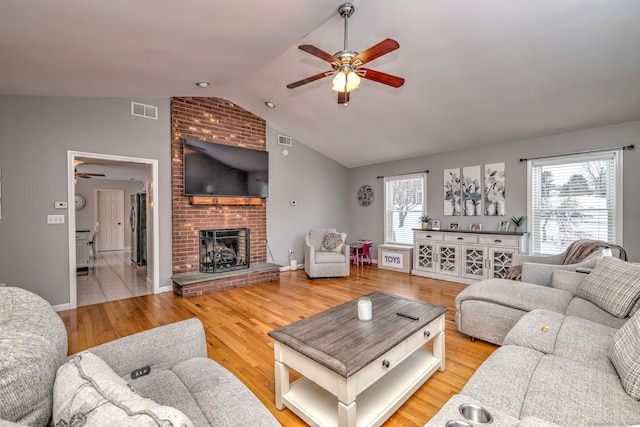 living room with a brick fireplace, plenty of natural light, wood-type flooring, and lofted ceiling