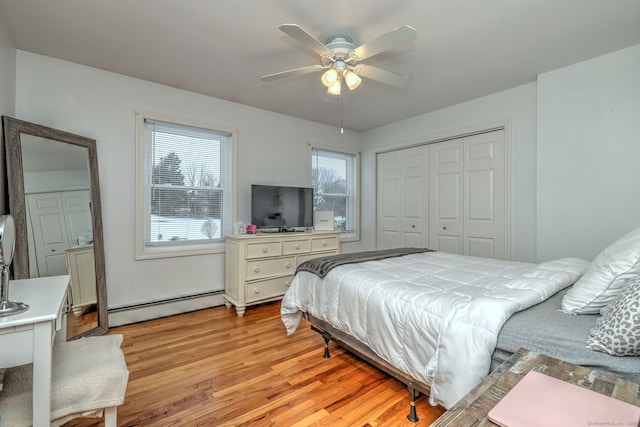 bedroom featuring ceiling fan, light hardwood / wood-style floors, multiple windows, and a baseboard heating unit