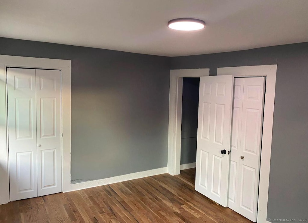 unfurnished bedroom featuring dark wood-type flooring and two closets