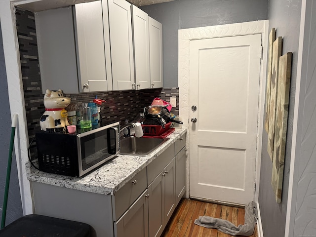 kitchen with dark hardwood / wood-style floors, gray cabinets, decorative backsplash, sink, and light stone countertops