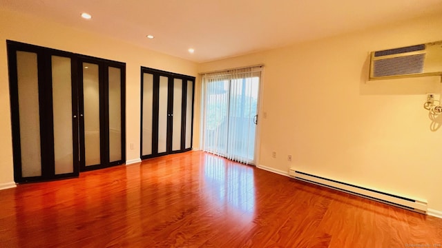 unfurnished room featuring a wall mounted air conditioner, hardwood / wood-style floors, and a baseboard radiator