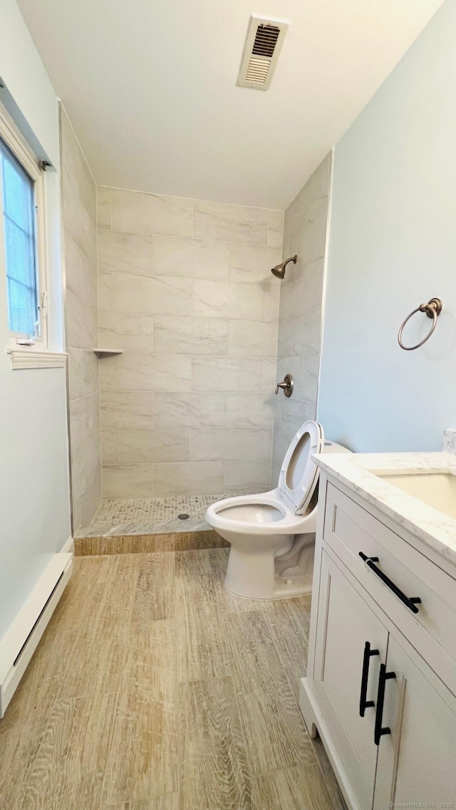 bathroom with toilet, a tile shower, hardwood / wood-style flooring, a baseboard radiator, and vanity