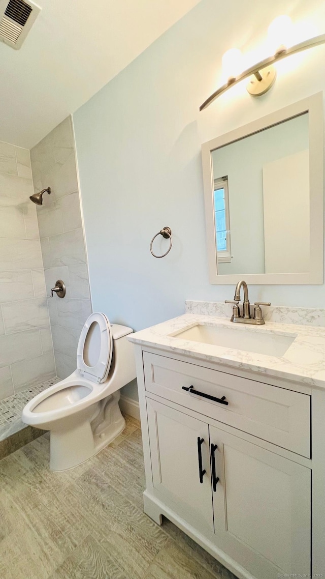 bathroom with tiled shower, vanity, and toilet