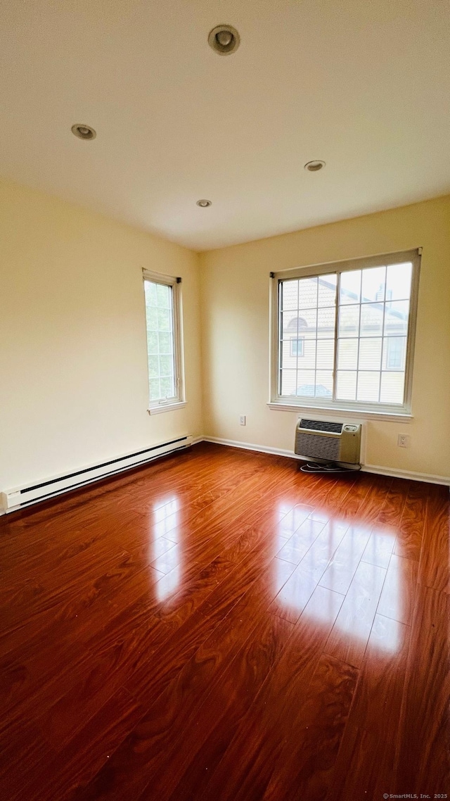 empty room with baseboard heating, a wealth of natural light, hardwood / wood-style flooring, and a wall unit AC