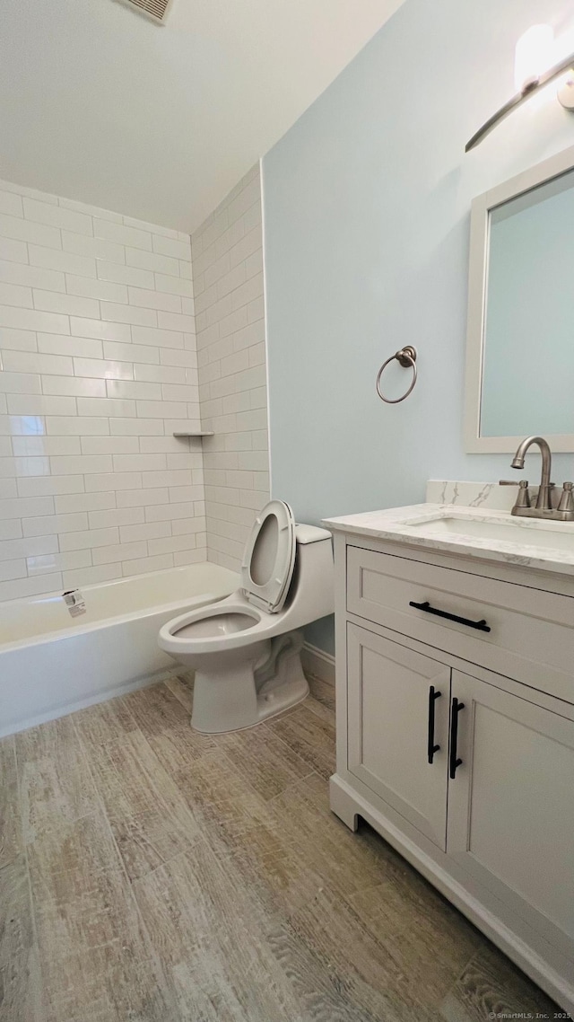 full bathroom with toilet, tiled shower / bath, hardwood / wood-style flooring, and vanity