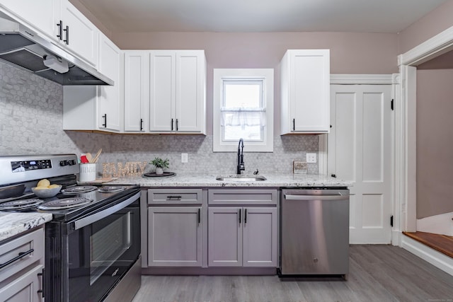 kitchen with appliances with stainless steel finishes, sink, white cabinets, light stone countertops, and light wood-type flooring