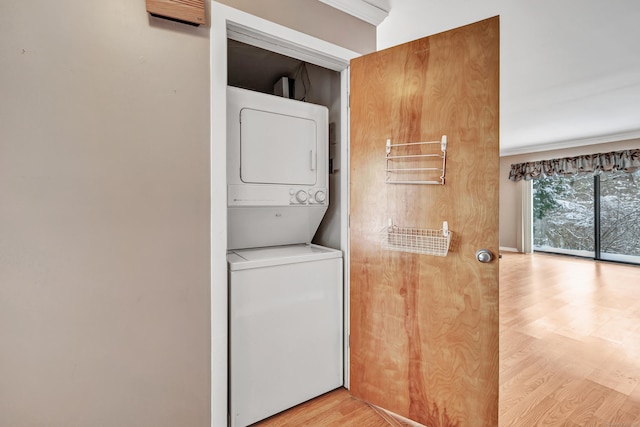 clothes washing area featuring stacked washer / dryer, ornamental molding, and light hardwood / wood-style floors