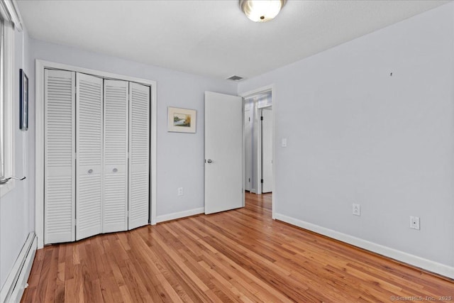 unfurnished bedroom with light hardwood / wood-style floors, baseboard heating, and a closet