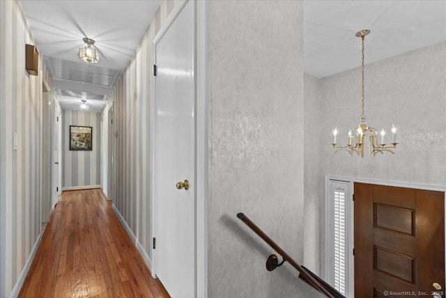 corridor with wood-type flooring and a notable chandelier