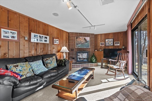 living room with a brick fireplace, rail lighting, wooden walls, and a healthy amount of sunlight