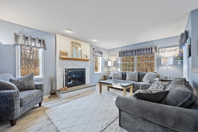 living room with a brick fireplace, a textured ceiling, and light hardwood / wood-style flooring