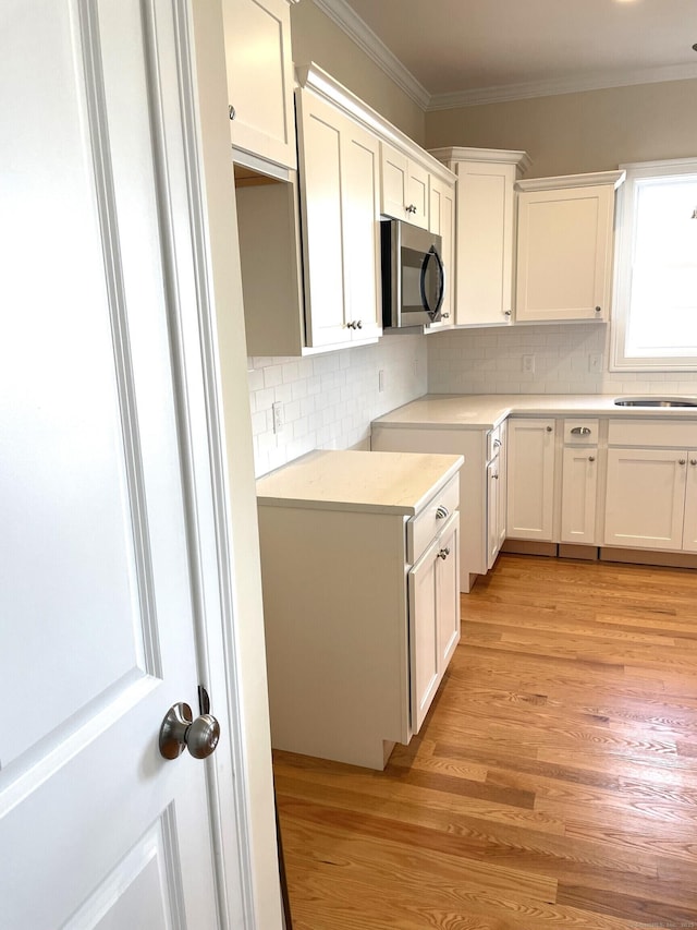 kitchen featuring backsplash, ornamental molding, light wood-type flooring, and white cabinets