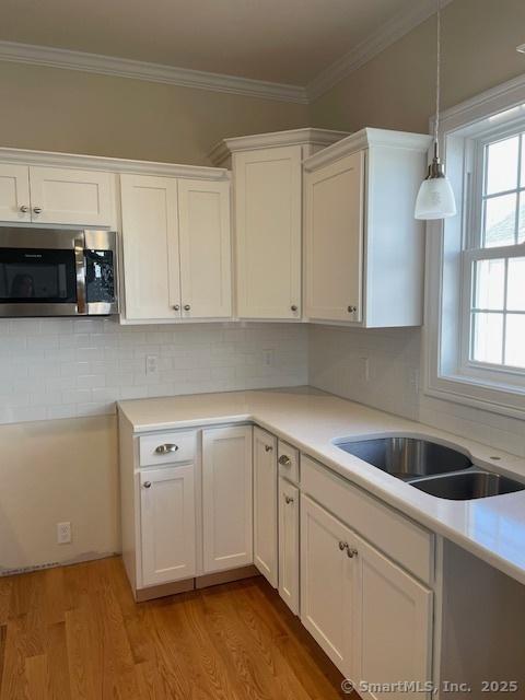 kitchen with pendant lighting, white cabinetry, sink, ornamental molding, and light hardwood / wood-style flooring