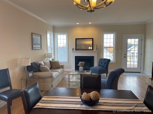 living room with an inviting chandelier, crown molding, plenty of natural light, and light hardwood / wood-style flooring