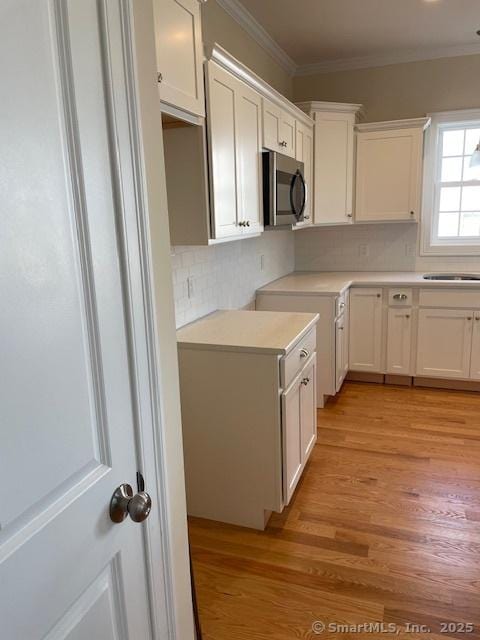 kitchen featuring crown molding, decorative backsplash, light hardwood / wood-style flooring, and white cabinets