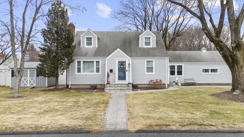 new england style home featuring a front yard and an outbuilding