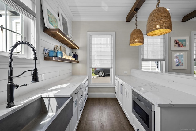 kitchen with stainless steel microwave, beam ceiling, white cabinets, and decorative light fixtures