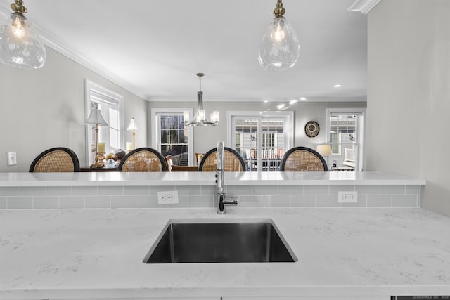 kitchen featuring light stone counters, sink, pendant lighting, and ornamental molding