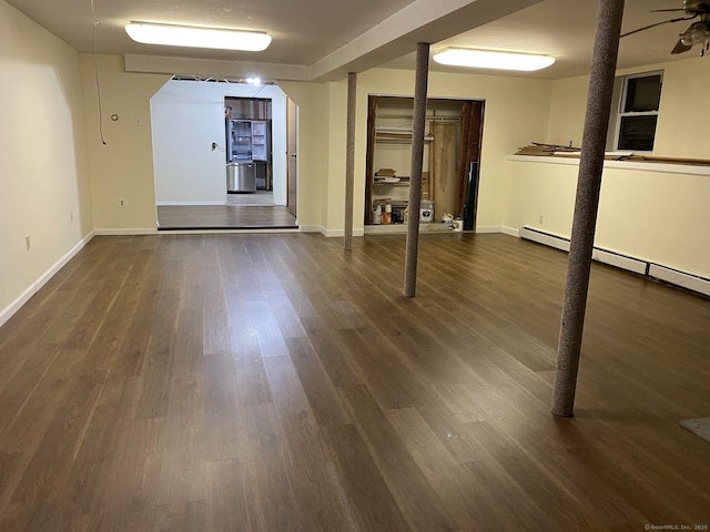 basement with ceiling fan, a baseboard heating unit, and dark hardwood / wood-style floors