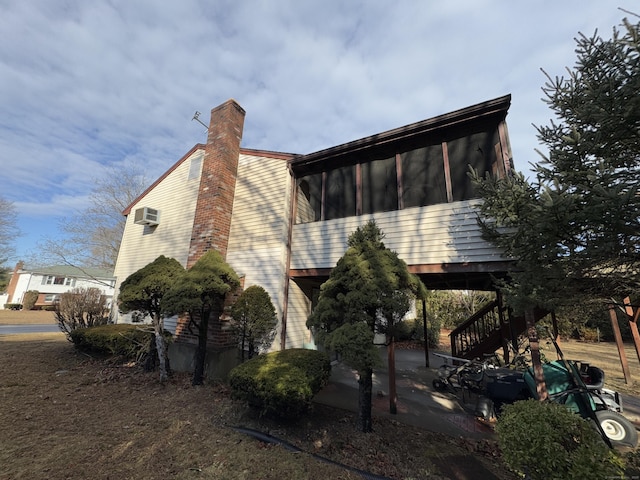 view of side of property featuring a wall unit AC, a patio, and a sunroom