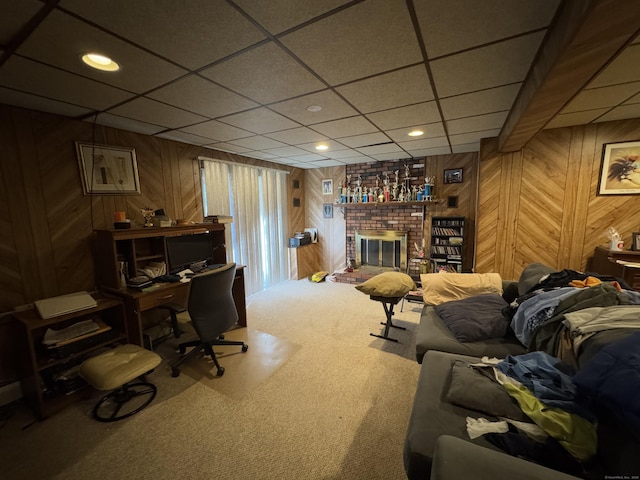 carpeted home office with a paneled ceiling, a brick fireplace, and wood walls