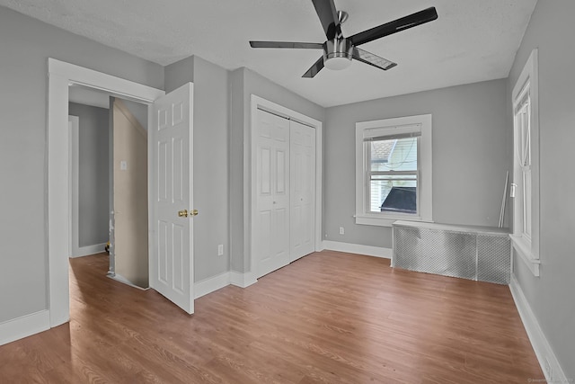 unfurnished bedroom featuring a textured ceiling, radiator, a closet, light wood-type flooring, and ceiling fan