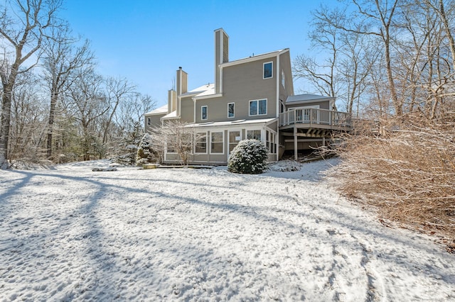 snow covered back of property with a wooden deck and a sunroom