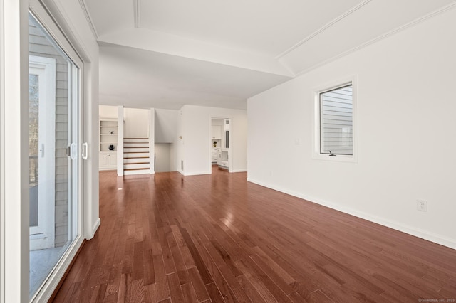 unfurnished living room with a healthy amount of sunlight, dark wood-type flooring, vaulted ceiling, and ornamental molding