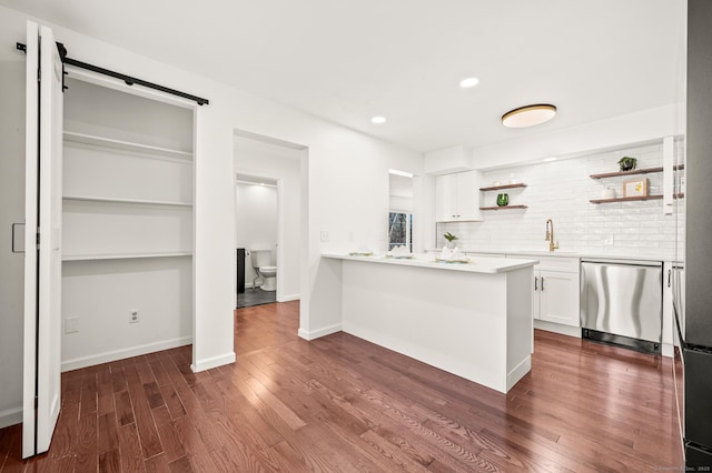 kitchen with a barn door, stainless steel dishwasher, white cabinets, kitchen peninsula, and dark wood-type flooring