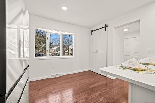 interior space featuring a barn door, dark hardwood / wood-style flooring, and stainless steel refrigerator