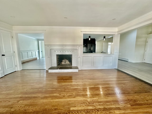 unfurnished living room with baseboard heating, ornamental molding, a brick fireplace, and light wood-type flooring