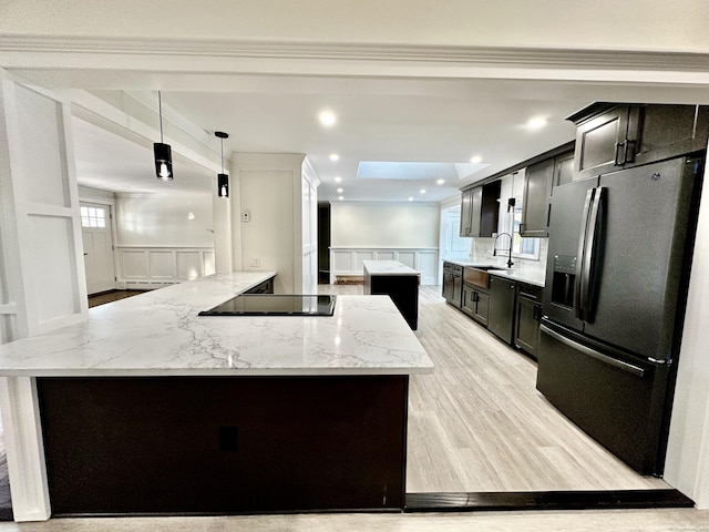 kitchen with a center island, stainless steel refrigerator with ice dispenser, light stone counters, black electric stovetop, and decorative light fixtures