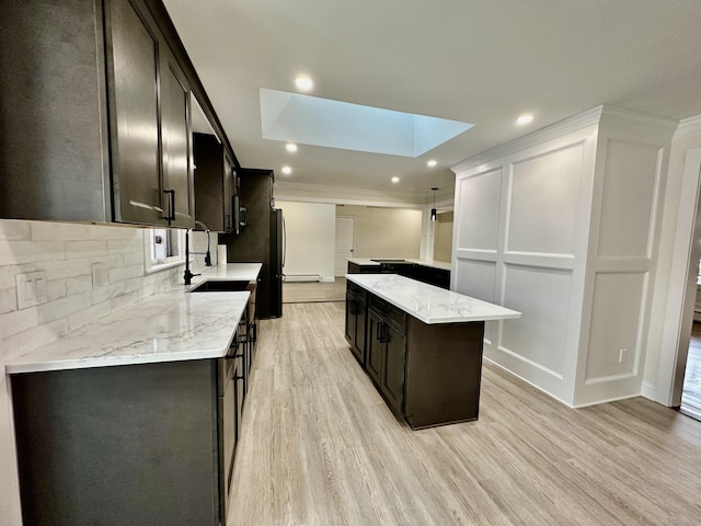 kitchen with a skylight, sink, a center island, light stone countertops, and light hardwood / wood-style flooring