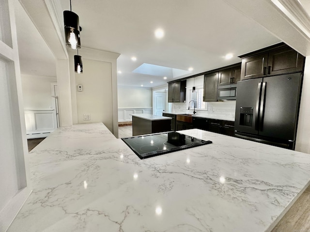 kitchen featuring sink, stainless steel fridge, a center island, light stone countertops, and black electric cooktop